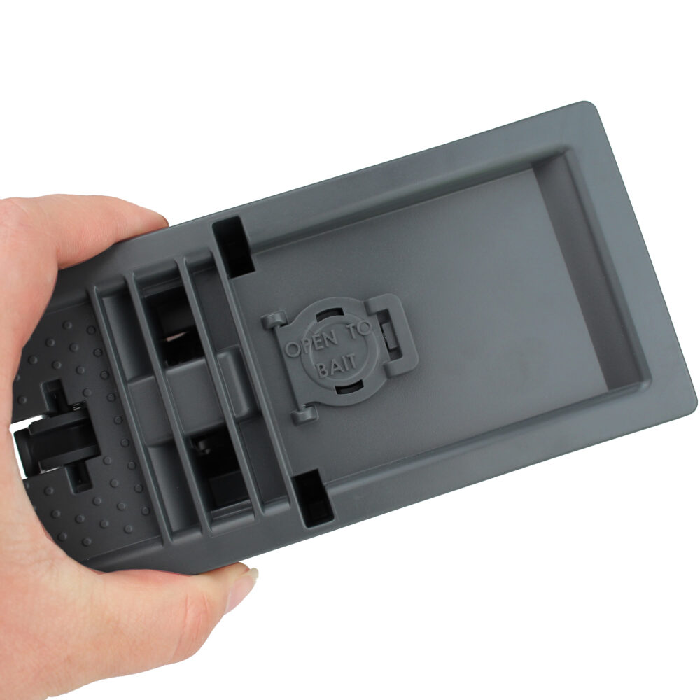 Grå råttfälla hålls i en hand, visas stängd och klar att användas.